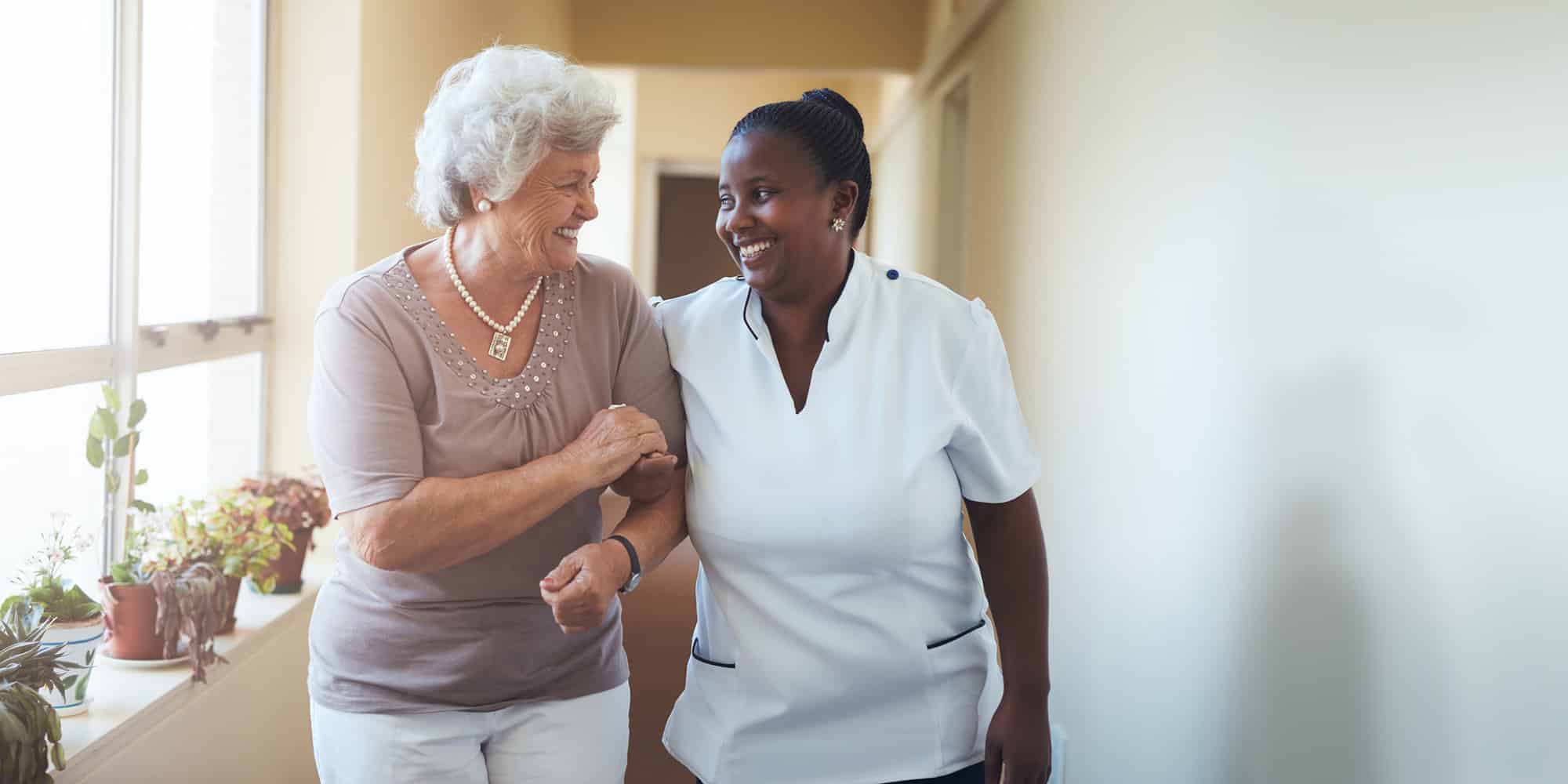 Nurse and resident walking arm in arm down the corridor